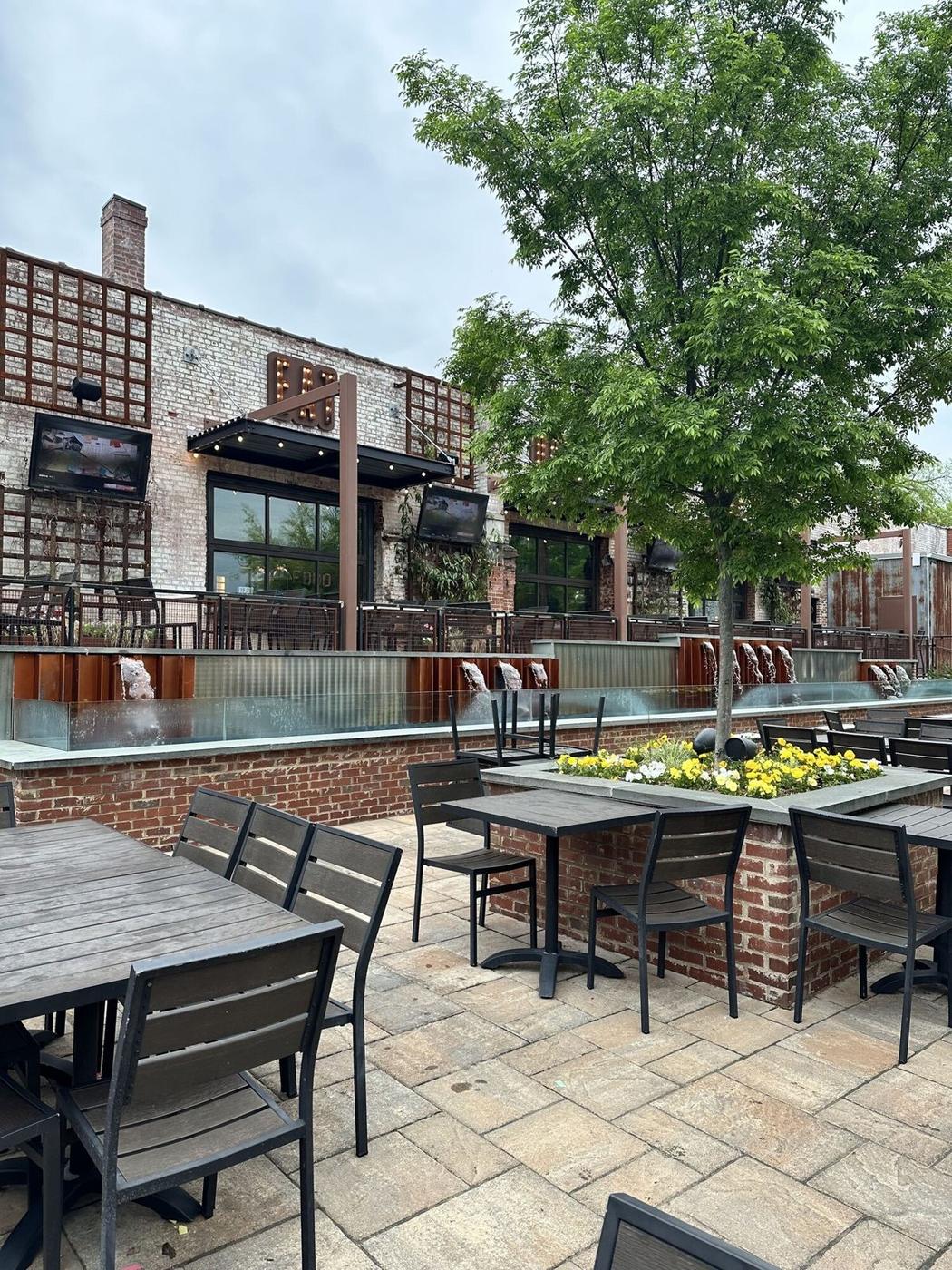 Brick restaurant patio with outdoor tables, a flowering planter and a shade tree in Downtown Greensboro, a short walk from the townhome